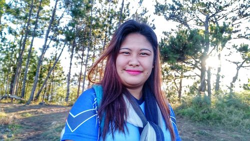 Portrait of smiling young woman standing against trees