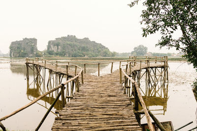 From above of wooden forked bridge on calm lake among green trees with island on background in vietnam