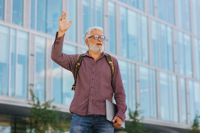 An adult man with a laptop outside the office. gray-haired senior businessman waves to colleagues