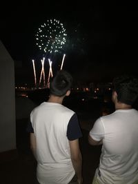 Rear view of people watching firework display at night