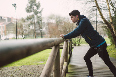 Side view of young man looking at railing against trees