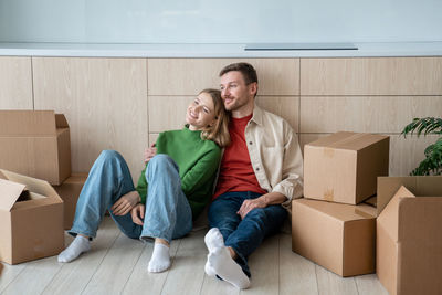 Happy couple man woman hugging dreaming about life in new apartment sitting on floor