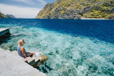 Woman sitting on rock by sea against sky