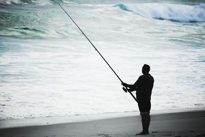 Silhouette man fishing on beach