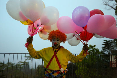 Clown holding multi colored balloons against sky