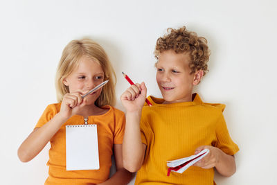 Siblings with pen and note pad sitting against white background
