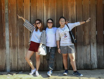 Full length portrait of sisters standing with mother against wooden fence