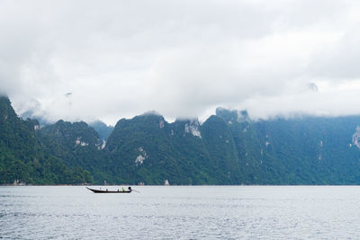 Sailboat sailing on sea by mountains against sky