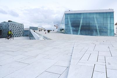 People on footpath by modern buildings against sky in city