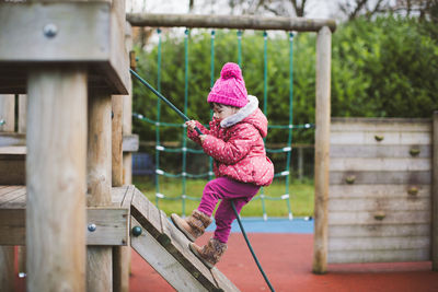 Side view of girl climbing with rope in playground