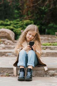 Caucasian girl of seven years old sits on stone steps in a park and communicates online with friends