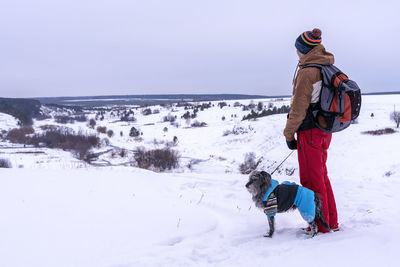 Man with mixed breed dog in warm blue suit walking in snow mountain looking at view in winter