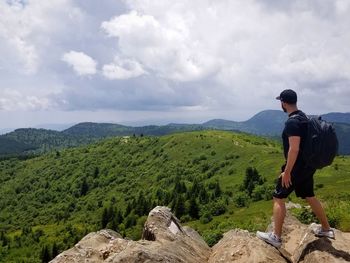 A young man hiking on the edge of a cliff overlooking the rolling green hills below