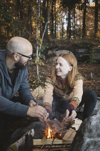 Smiling couple making campfire in forest