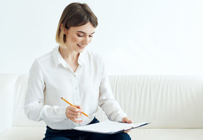 Smiling businesswoman writing on document sitting on sofa