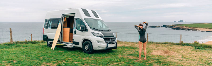 Young woman closing the zipper of her wetsuit for surfing next to her camper van