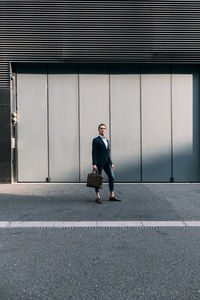 Businessman holding briefcase while standing on footpath