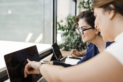 Happy businesswoman pointing at laptop by colleague in office