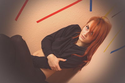 High angle portrait of redhead young woman sitting by wall