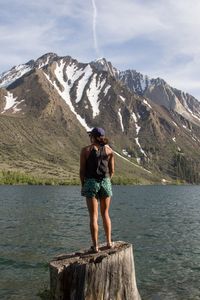 Rear view of woman standing on tree stump by lake