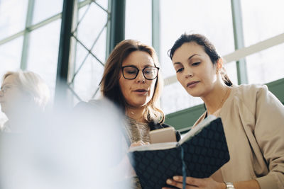 Businesswomen discussing over diary while using smart phone at office meeting