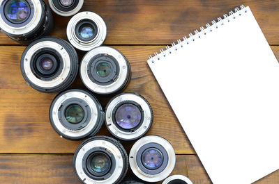 High angle view of camera lens with note pad on wooden table