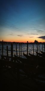 Silhouette wooden posts in sea against sky during sunset