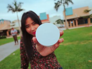 Portrait of young woman holding powder compact on field