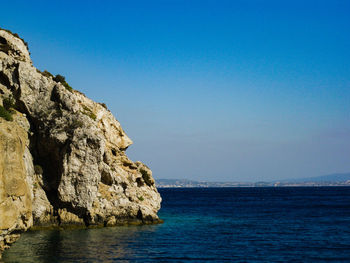 Rock formation in sea against clear blue sky