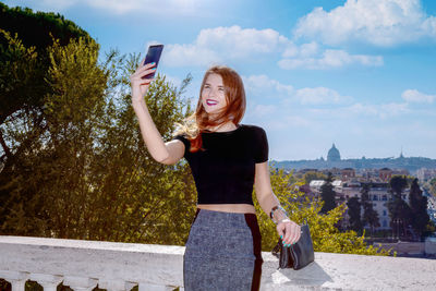 Rear view of young woman with arms raised standing against sky