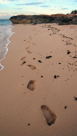 Footprints on sand at beach against sky