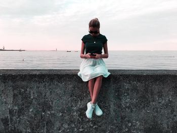 Rear view of young woman standing at beach against sky