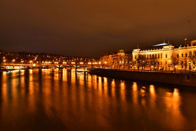 Illuminated buildings by river against sky at night