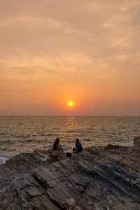 Silhouette couple sitting on beach against sky during sunset
