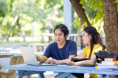 Couple of students sitting and using laptop in outdoor university doing some online research