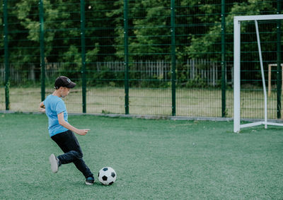 The boy on the football field kicks the ball. the boy runs on the green lawn for the ball