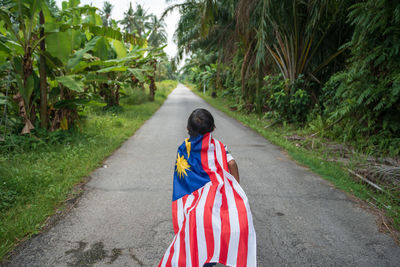 Rear view of boy with malaysian flag walking on road 