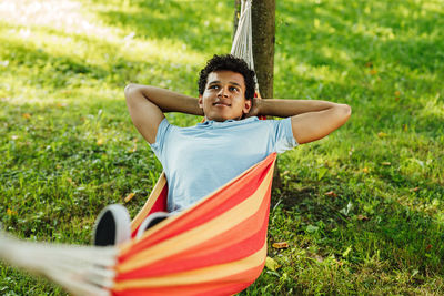 Young man looking away while relaxing in hammock at park