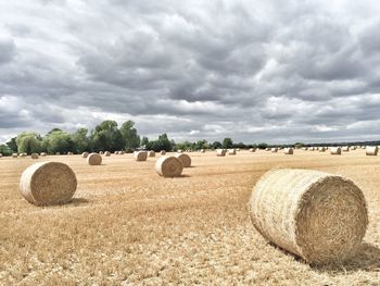 Hay bales on field against cloudy sky