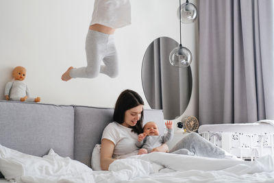 Mama with two kids at home in bedroom. baby infant resting on mothers hands, while older sister