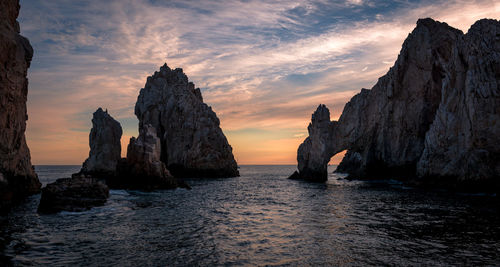 Rock formations in sea against cloudy sky during sunset