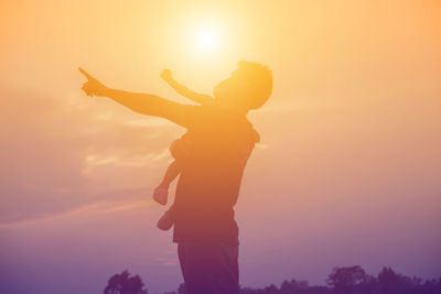 Silhouette man standing by orange sun against sky during sunset