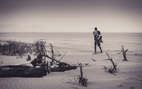 Rear view of man walking on sand against sea at beach