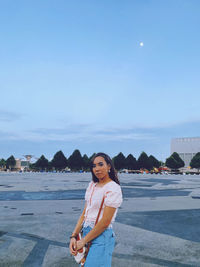 Portrait of young woman standing on beach against sky