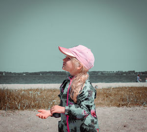 Girl wearing cap while standing at beach against sky