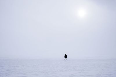 Distant view of silhouette person standing on snow covered field