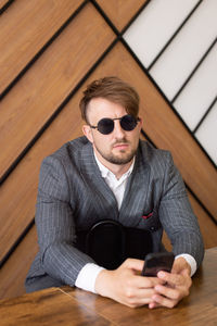 A young man in a suit and sunglasses is sitting in the office and looking at the phone