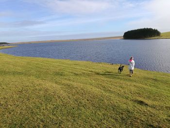 Rear view of boy with dog walking on field against lake