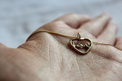 Close-up of cropped hand showing necklace with love text pendant