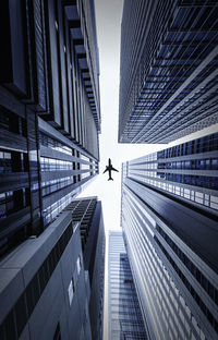 Directly below shot of modern buildings and airplane against sky